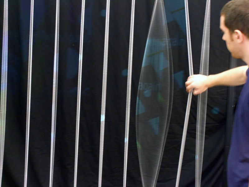 A visitor interacting with the Logtime Twister, pulling one of the vertical strings to reveal a projection
