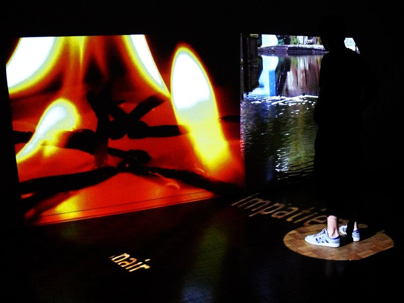 A visitor standing inside a projected circle on the floor of the Oracle installation, with a word visible on the parquet