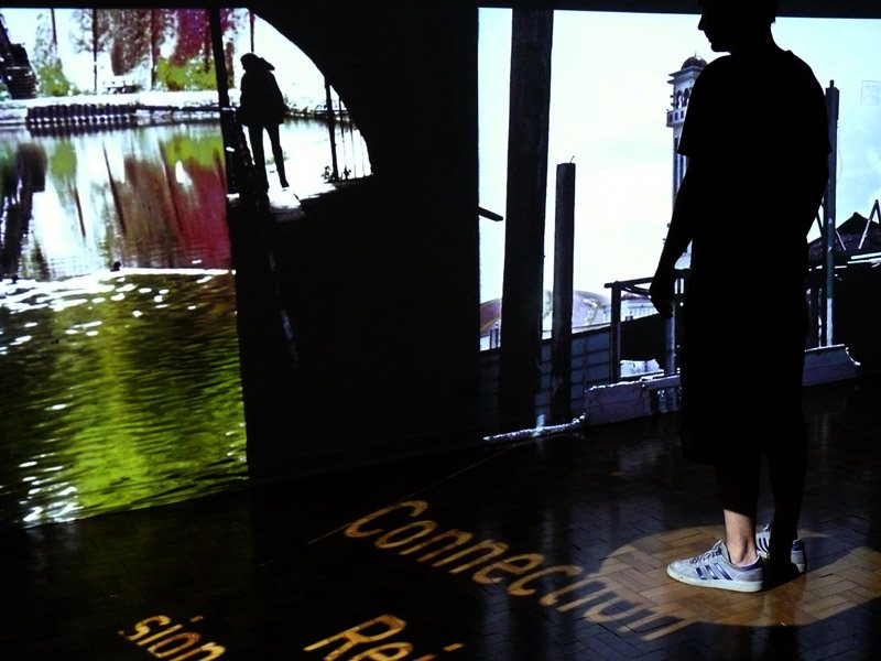 The Oracle installation with a visitor silhouetted against video projections and floor text